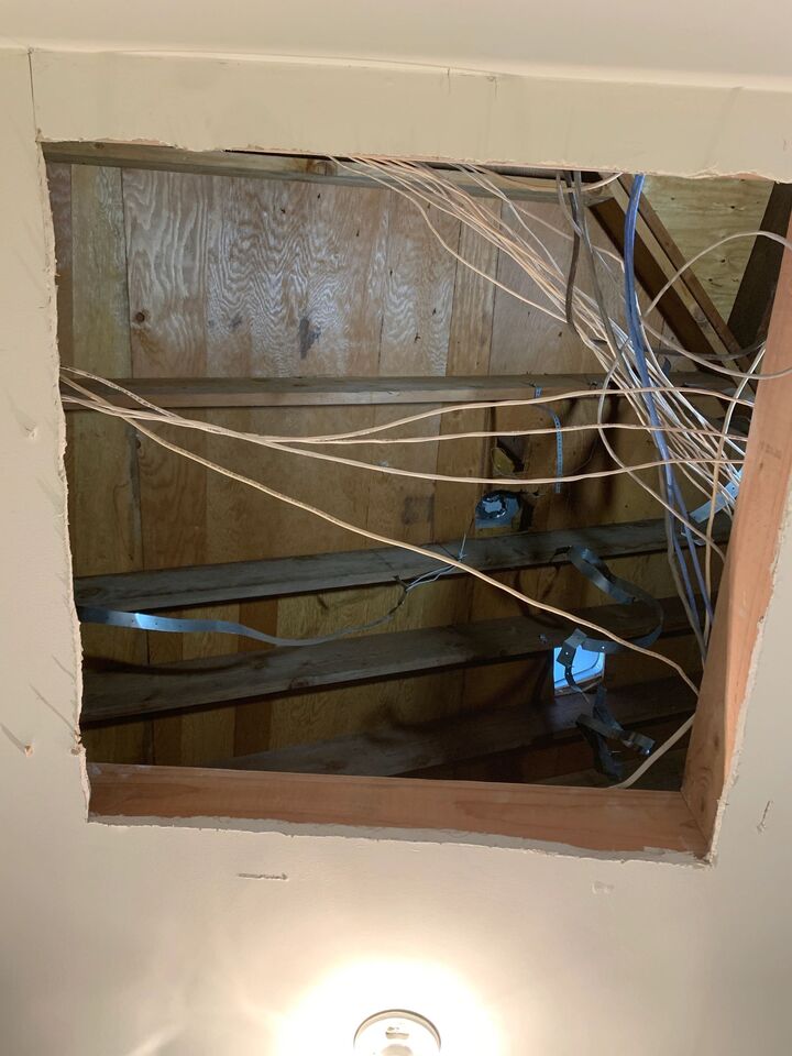 New attic opening cut into a ceiling showing the framed edge and existing wiring running through the joist bay
