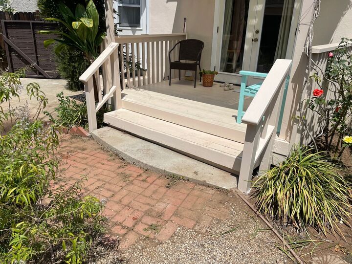 Rebuilt front porch with pale painted steps and railing meeting a brick pathway