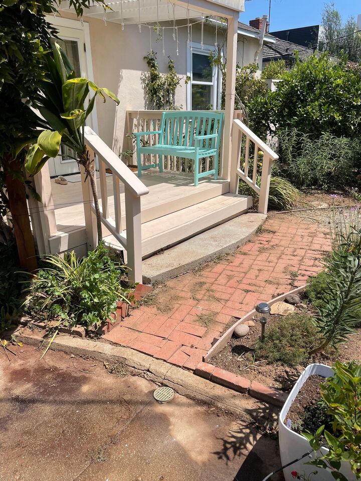 Front porch and steps with a pale painted rail, brick path and mature planting