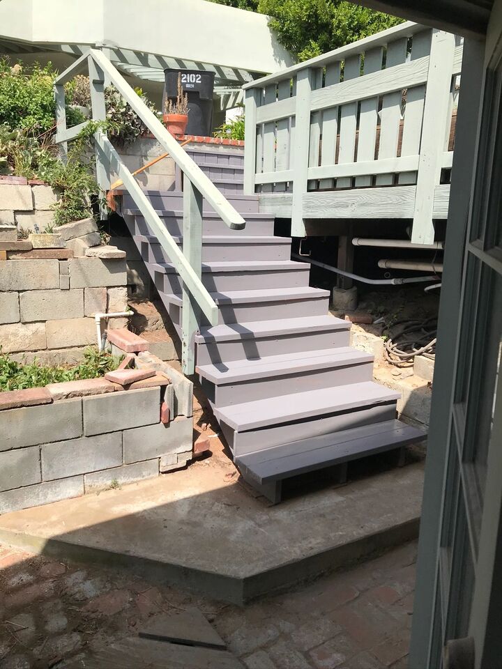 Long flight of exterior steps with grey treads and a metal handrail against a block wall