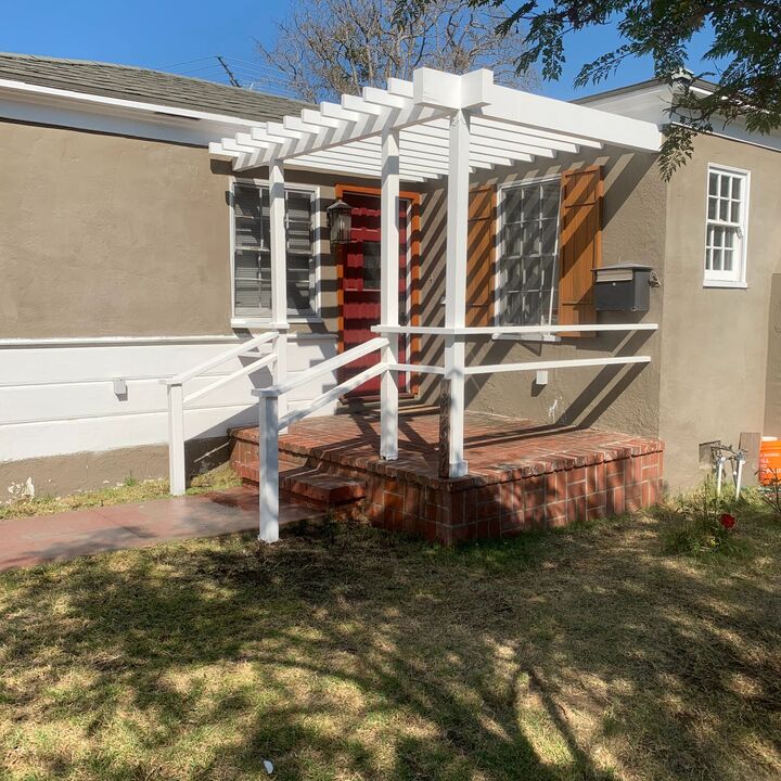 White pergola over a raised deck at the side of a house with a lawn in front