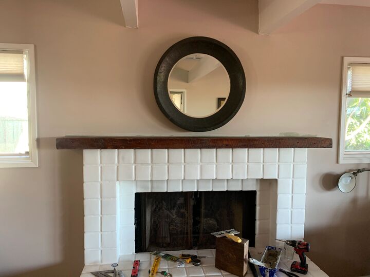 Dark timber mantle shelf fitted across a white painted brick fireplace with a round mirror above