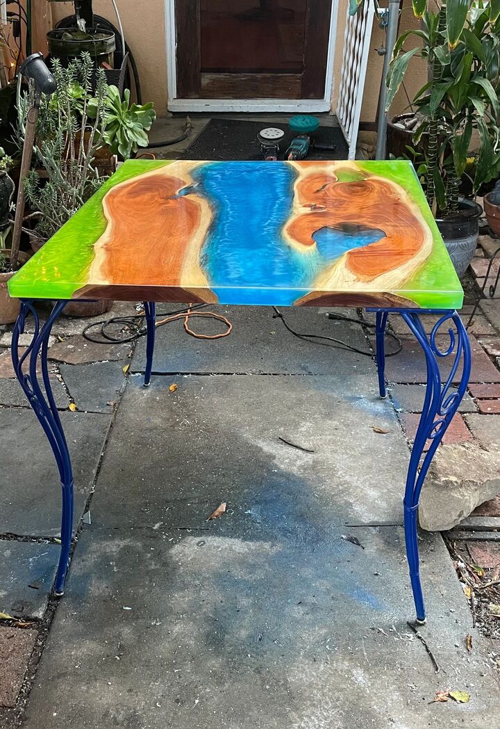 Finished green and blue resin table top on ornate blue iron legs standing on a patio