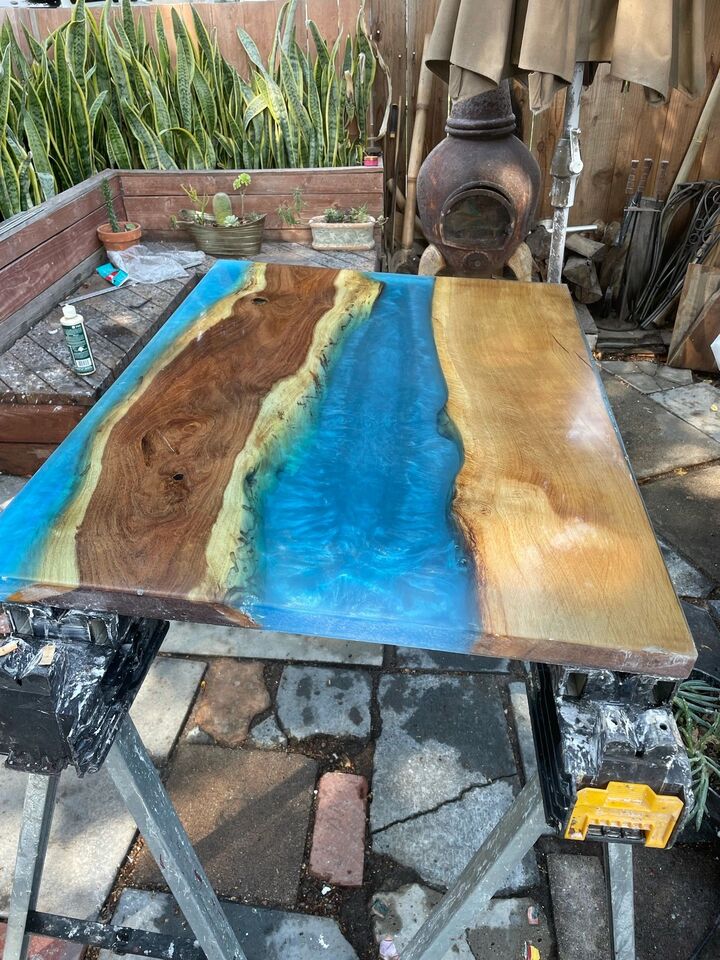Resin table top curing on trestles outdoors, showing the bright green and blue river between the wood