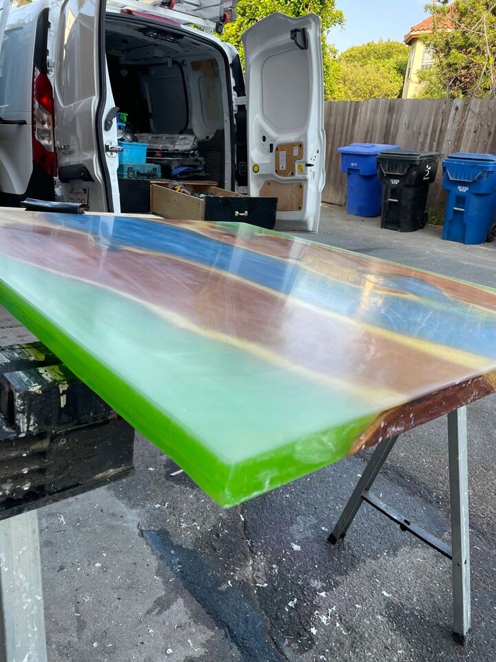 Green resin table top on folding trestles beside a work van, viewed down its length