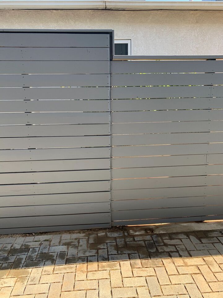 Horizontal fence panels fixed to slim grey steel posts beside a paved driveway