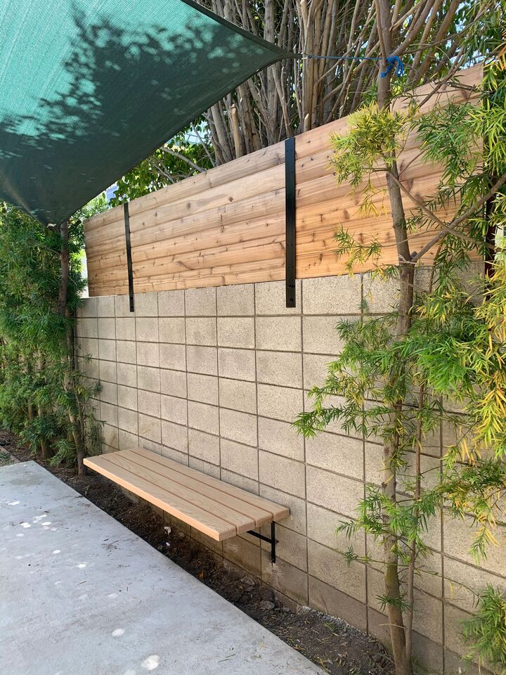 Redwood fence panel on steel posts raising the height of an existing block wall, with a bench below