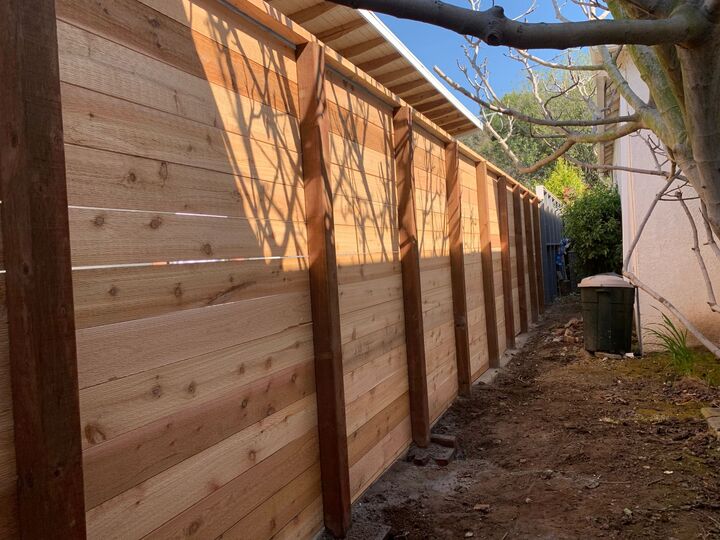 Tall horizontal redwood fence running along a side yard with even gaps between every board