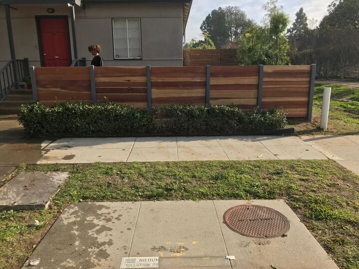 Horizontal redwood fence along a front lawn with a concrete walkway in the foreground