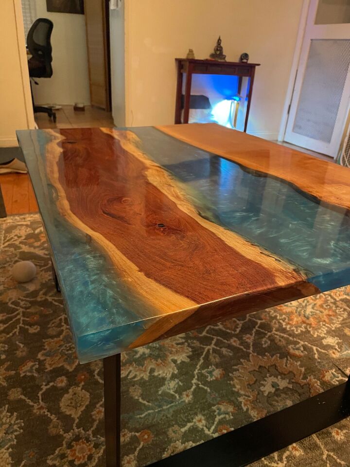 Live-edge walnut dining table with a clear blue resin river down the centre, on a patterned rug in a bright room