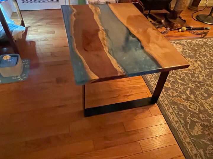 Live-edge river table on a dark steel base viewed along its length on a hardwood floor