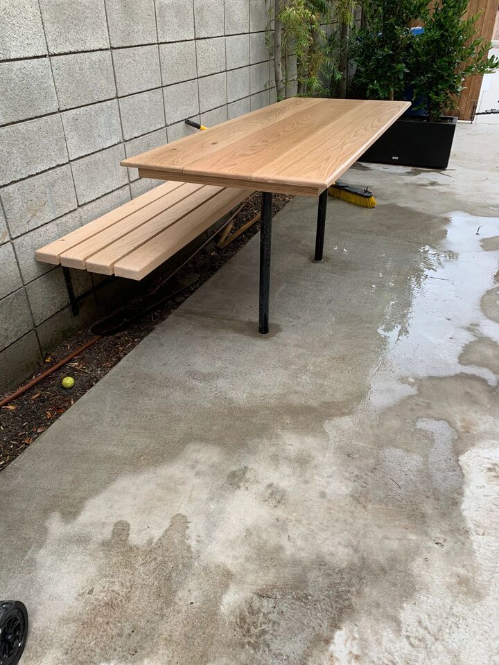 Pale hardwood table and matching wall bench on slim black steel frames against a block wall