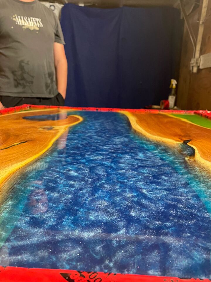 Deep blue and orange resin pour in progress on a protective sheet, with the maker working the surface