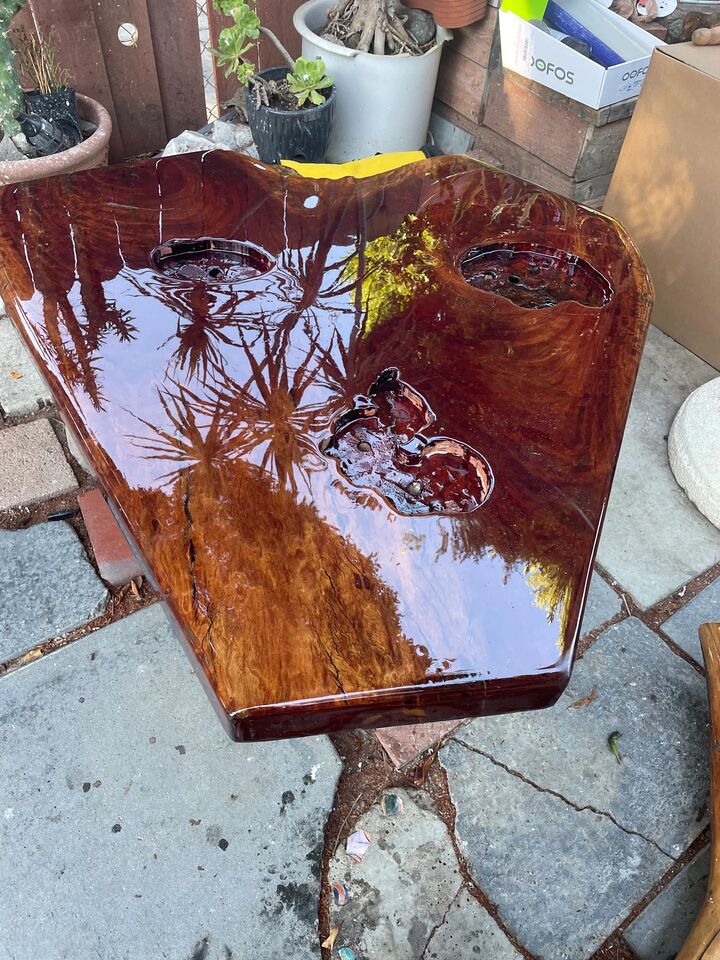 Dark red-brown resin and wood table top with a high-gloss finish standing on a stone patio
