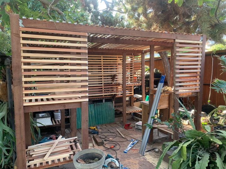 Slatted timber privacy screen and pergola frame under construction in a back garden