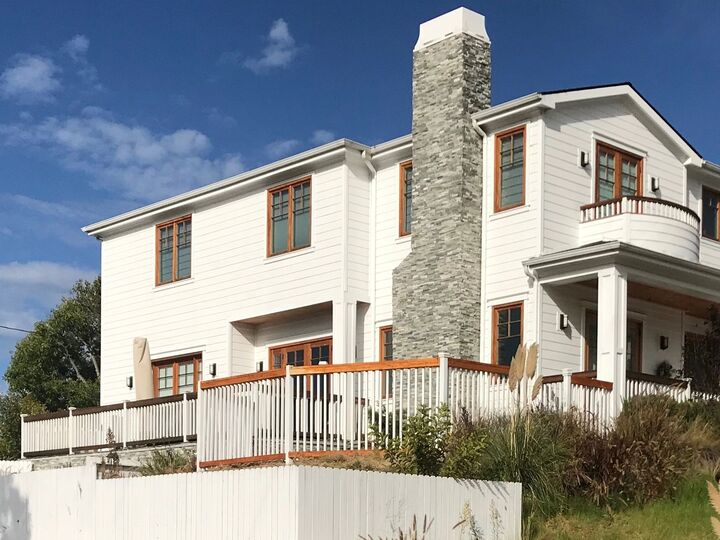 Two-storey house with a stone chimney, white railing and timber fencing at the front