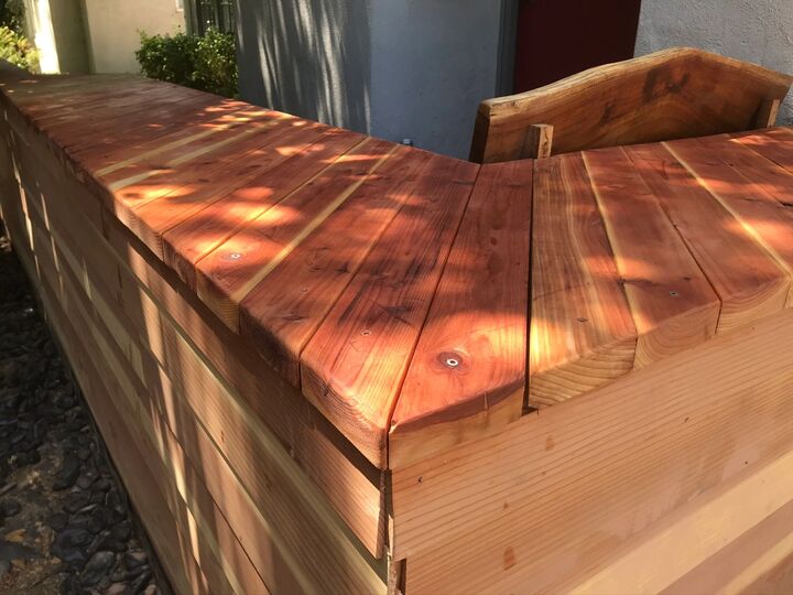 Sunlit close view of the redwood bench lid and armrest, showing the smooth sanded seat surface