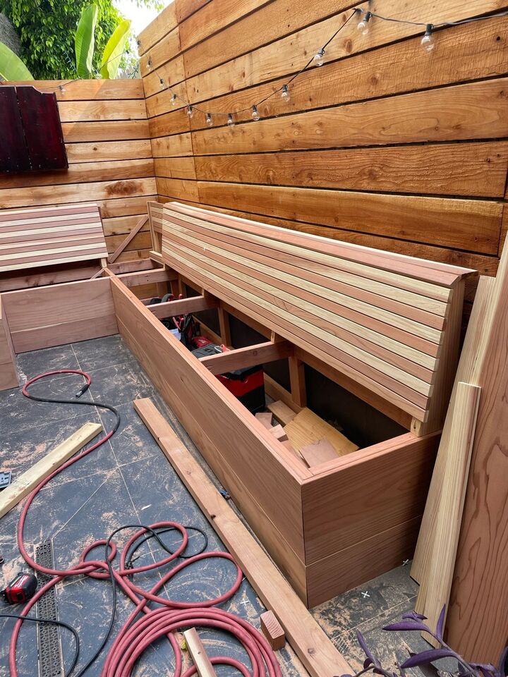 Bench construction in progress with redwood boards, clamps and an air hose on the patio floor