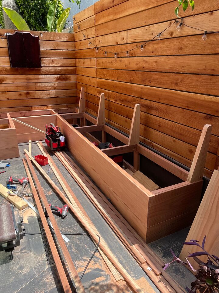 Partially built redwood bench frame with vertical supports in place and loose decking boards staged alongside