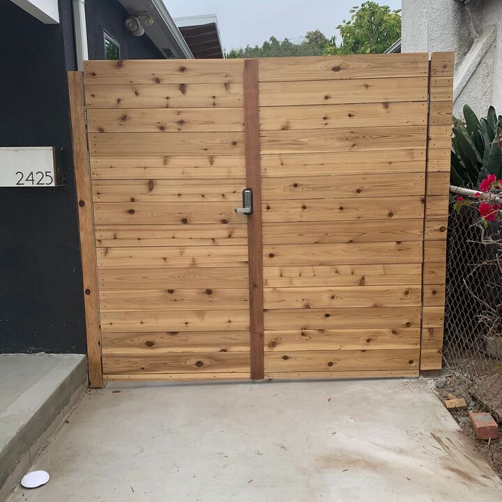 Pair of tall redwood gates closed across a concrete driveway opening