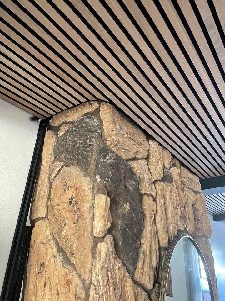 Timber slat ceiling running at a diagonal and scribed around a rough stone chimney breast