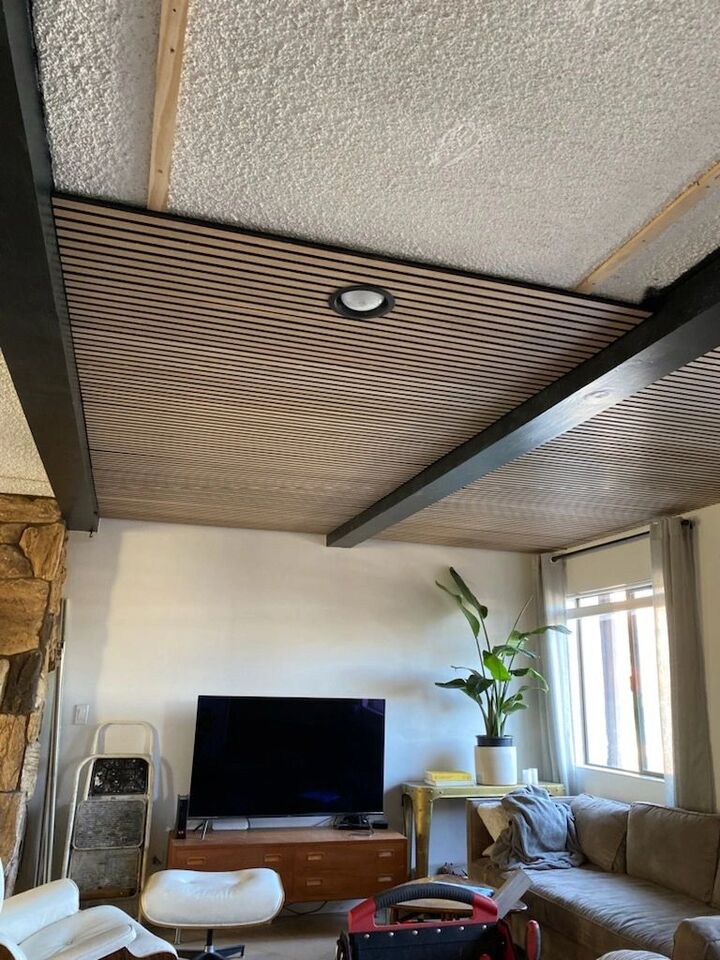 Slatted timber ceiling above a living room with recessed lighting and a window at the far end