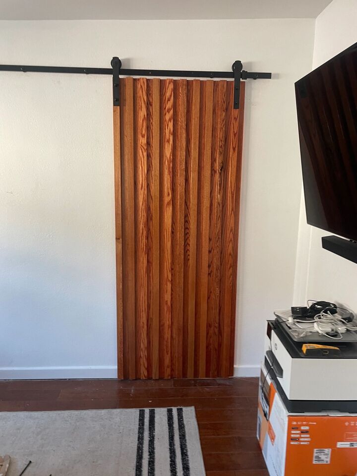 Sliding barn door in warm timber hung on black top track beside a wall-mounted television
