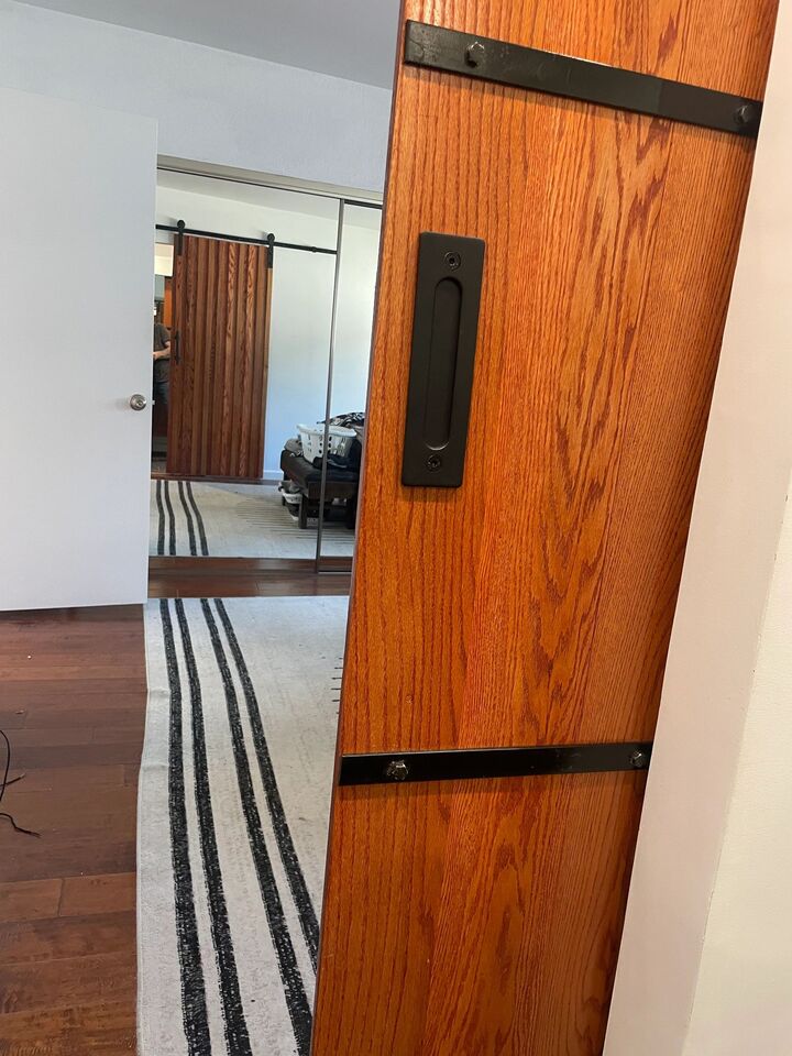 Timber barn door part-open with black strap hardware, showing the striped rug in the room beyond