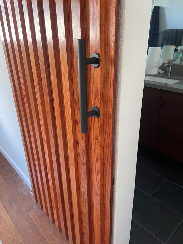 Slatted timber sliding door with a long black pull handle at the entrance to a bathroom