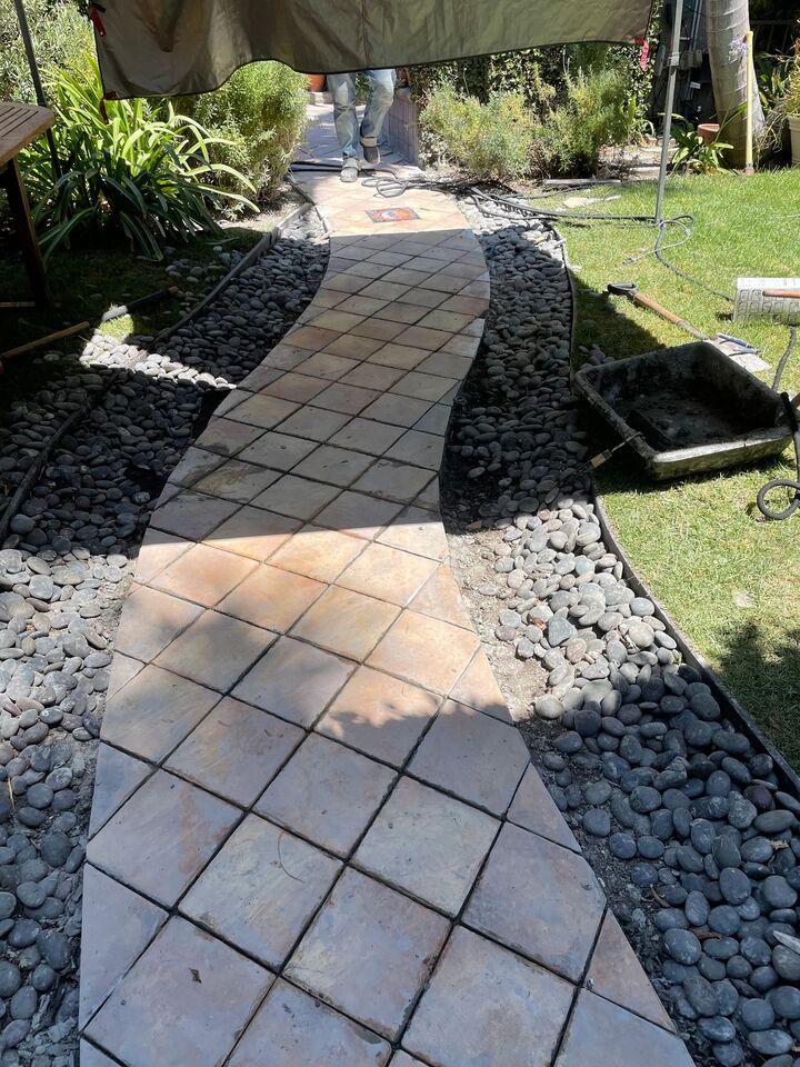 Diagonal tiled garden path set between dark pebble margins running across a lawn