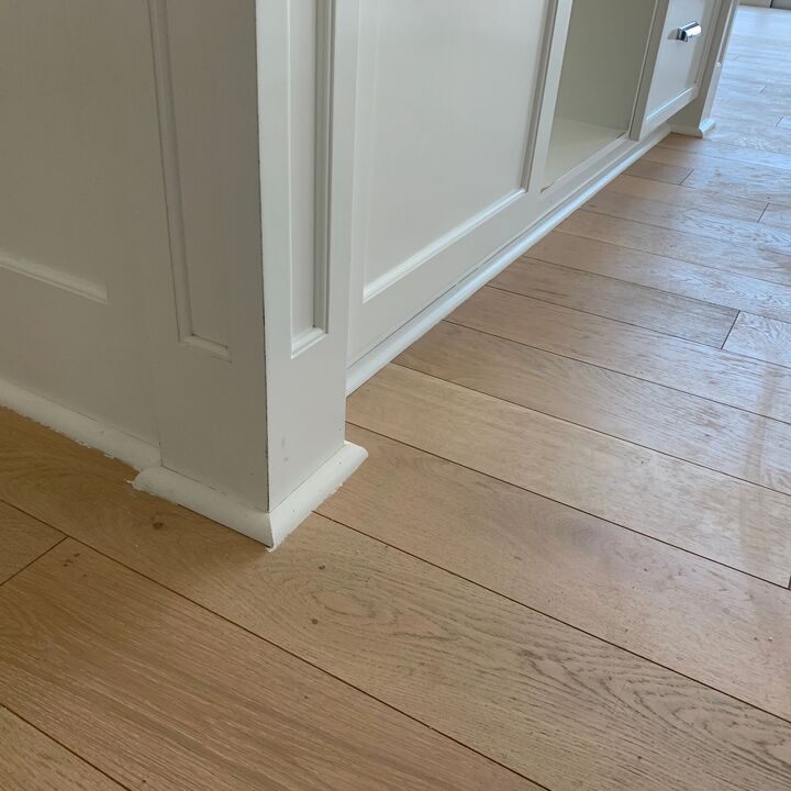 New white baseboard and cabinet trim running along a pale timber floor