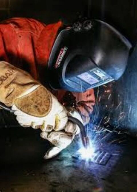 Welding in progress behind a welding helmet, with the arc lighting up the work and the visor reflection