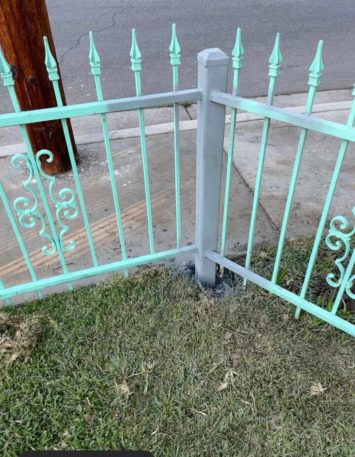 Repaired pale green wrought iron fence with spear tops and scroll detail standing on a lawn